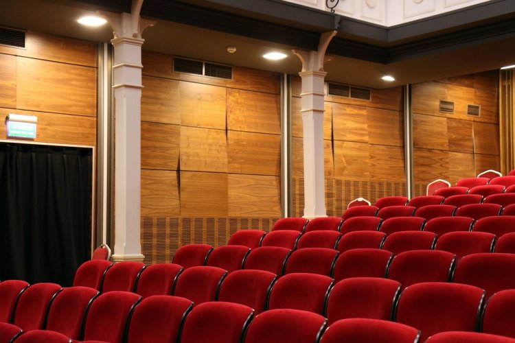 Photo of an empty theatre with red chairs.